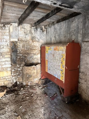 Distributeur vintage rouge dans une chambre d’hôtes à Angoulême, en Charente, avec des murs en pierre, des poutres apparentes et un sol d’époque.