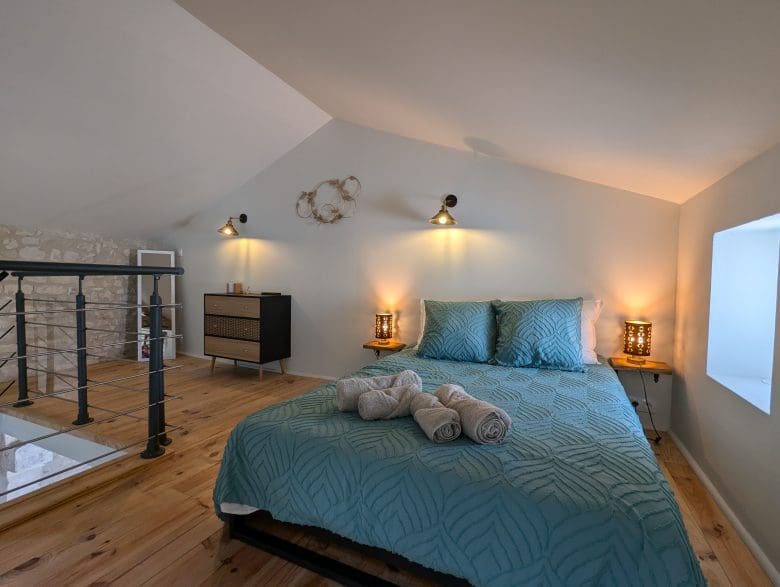 Une chambre d’hôtes chaleureuse aménagée dans les combles à Angoulême, avec un lit bleu canard, du bois de Charente, une lumière douce et des serviettes à votre disposition.