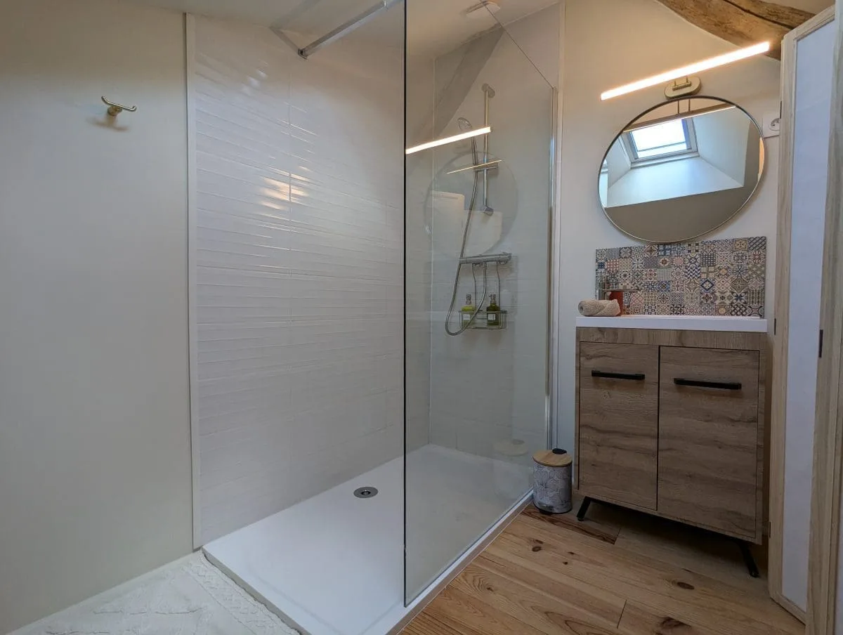 Salle de bains moderne et charmante à Angoulême, douche à l’italienne vitrée, bois clair, miroir rond, style charentais lumineux.