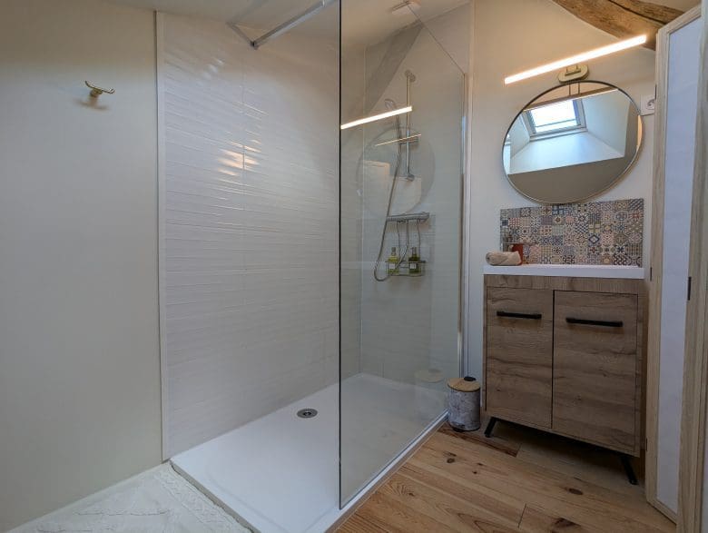 Salle de bains moderne et charmante à Angoulême, douche à l’italienne vitrée, bois clair, miroir rond, style charentais lumineux.