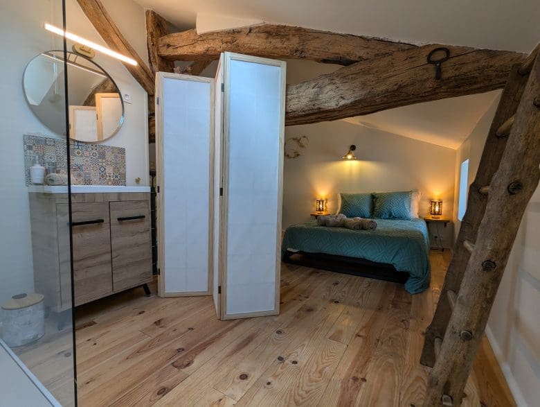 Chambre mansardée au charme charentais : poutres apparentes, lit double bleu canard, décoration en bois et lumière tamisée près d’Angoulême.
