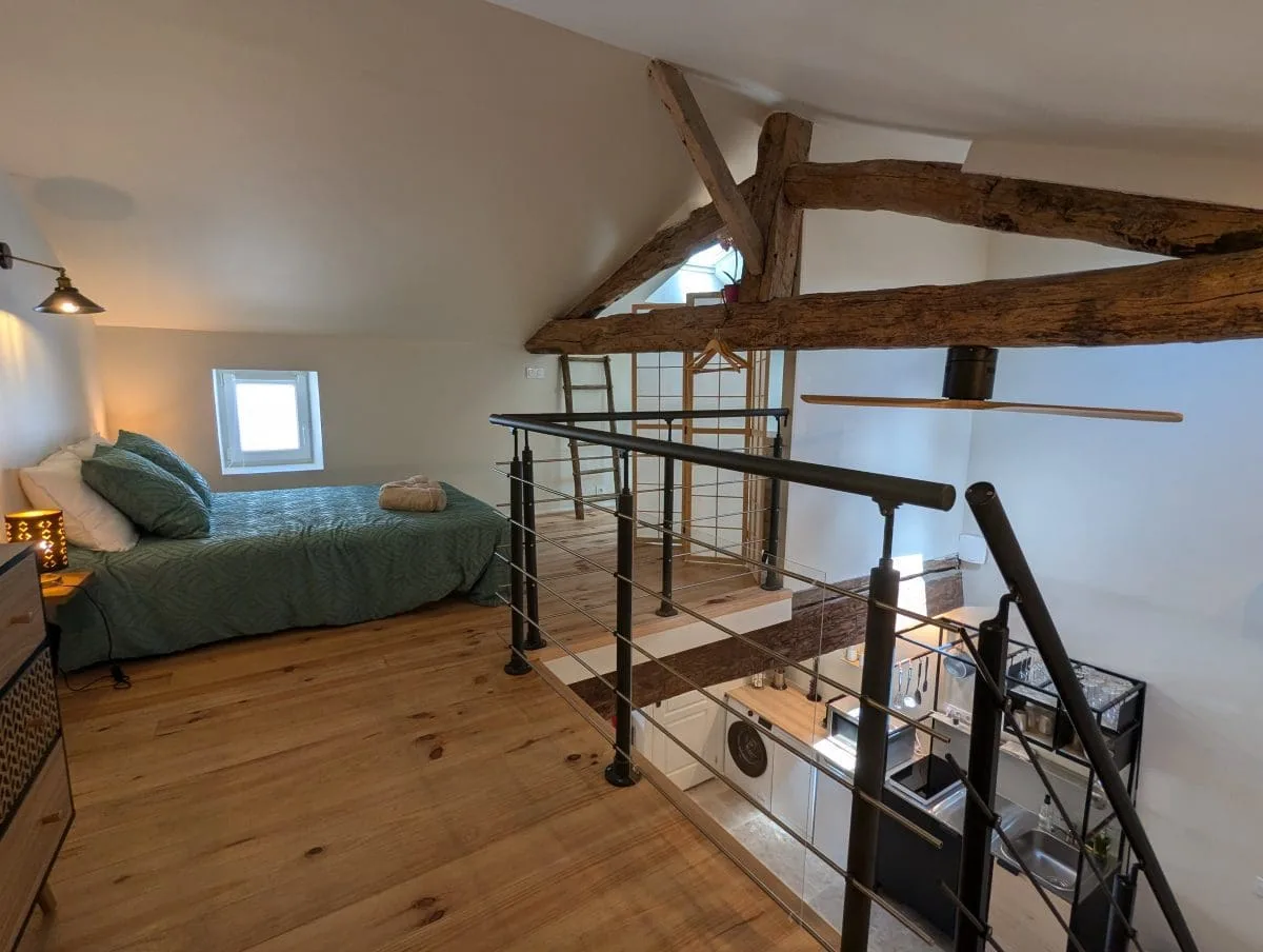 Chambre en mezzanine confortable à Angoulême, lit simple, poutres charentaises, parquet chaleureux, vue sur un espace ouvert moderne.