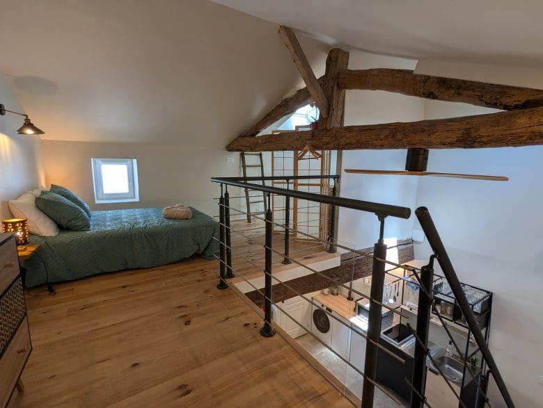 Chambre en mezzanine confortable à Angoulême, lit simple, poutres charentaises, parquet chaleureux, vue sur un espace ouvert moderne.