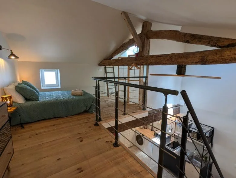 Chambre en mezzanine confortable à Angoulême, lit simple, poutres charentaises, parquet chaleureux, vue sur un espace ouvert moderne.