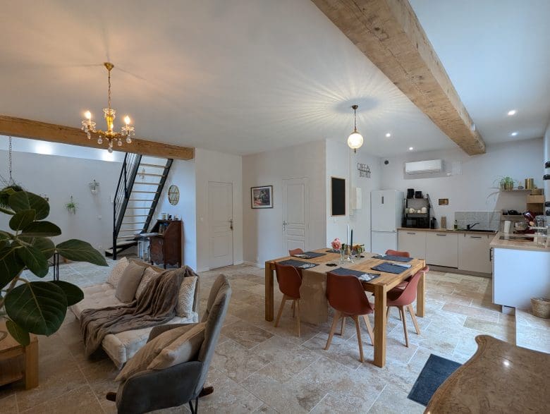 Séjour lumineux de style charentais à Angoulême, avec poutres apparentes, table en bois pour 6 personnes, cuisine équipée et escalier chaleureux.