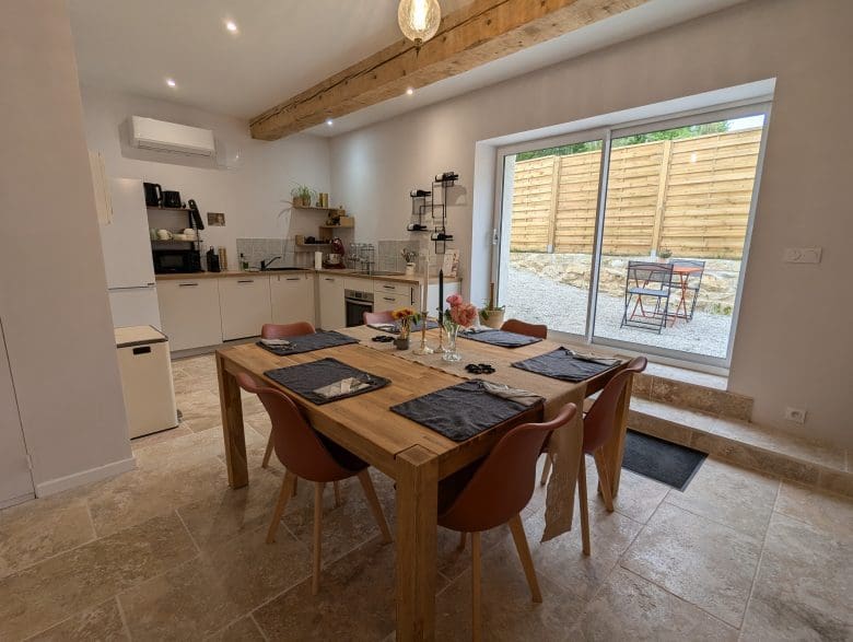Cuisine conviviale dans le style d’une maison d’hôtes en Charente, poutres apparentes, table pour 4 personnes, vue sur le patio à Angoulême, tons neutres et chaleureux.