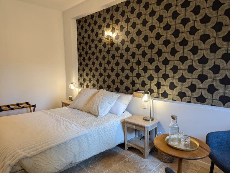 Chambre d’hôtes à Angoulême : lit soigné, mur au style charentais, lampes chaleureuses et carafe d’eau pour un séjour douillet.