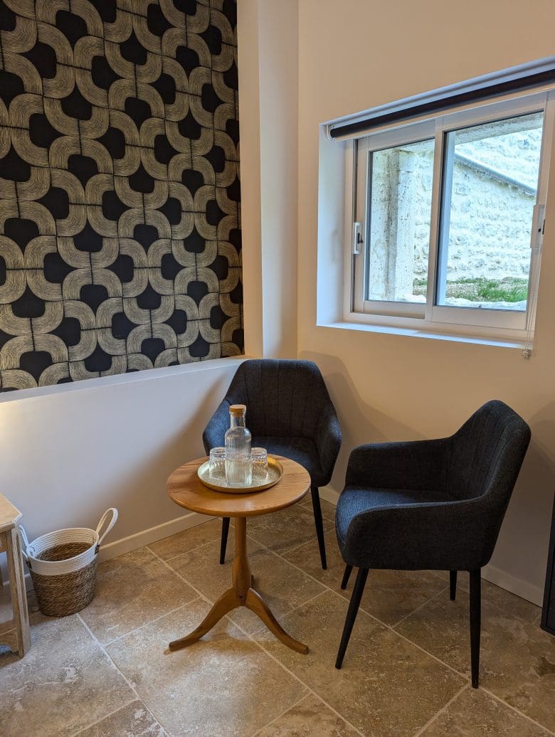 Un coin détente typique d’une maison d’hôtes en Charente, à Angoulême : deux fauteuils confortables, une table en bois, une carafe locale et une décoration raffinée.