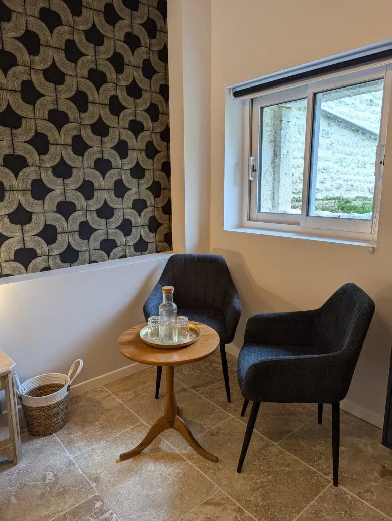 Un coin détente typique d’une maison d’hôtes en Charente, à Angoulême : deux fauteuils confortables, une table en bois, une carafe locale et une décoration raffinée.