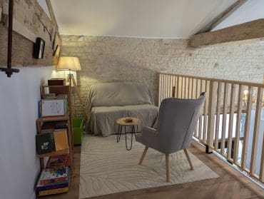 Un salon chaleureux, dans le style d’une maison d’hôtes à Angoulême : accoudoirs moelleux, murs en pierre de Charente, livres et jeux.
