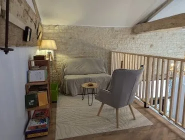 Un salon chaleureux, dans le style d’une maison d’hôtes à Angoulême : accoudoirs moelleux, murs en pierre de Charente, livres et jeux.