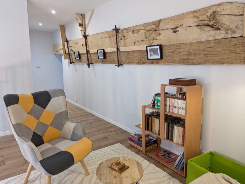 Salon chaleureux d'une maison d'hôtes en Charente, avec un fauteuil en patchwork, une table ronde, une étagère à livres et une poutre rustique à Angoulême.