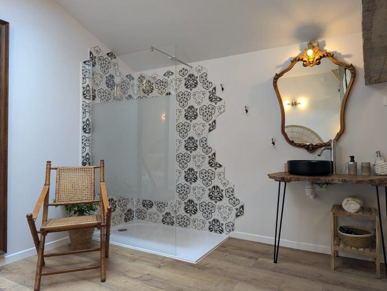 Élégante salle de bain inspirée des maisons d’hôtes charentaises à Angoulême, avec douche à l’italienne, carrelage à motifs et chaise vintage.