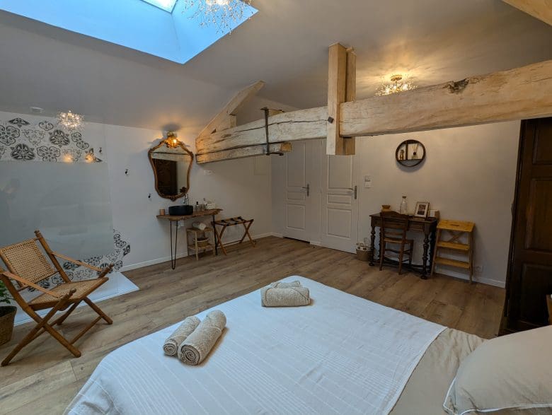 Chambre lumineuse à Angoulême avec poutres apparentes typiques de la Charente, lit double, serviettes, meubles vintage, parquet clair et ambiance chaleureuse.