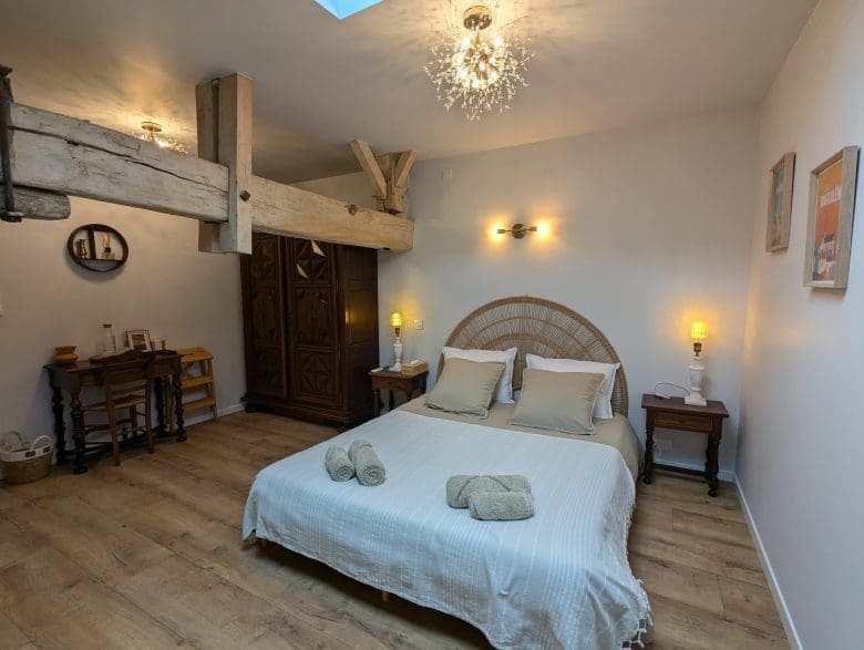 Chambre d’hôtes de charme à Angoulême : lit double, poutres charentaises, parquet, bureau, armoire en bois et lumière tamisée.