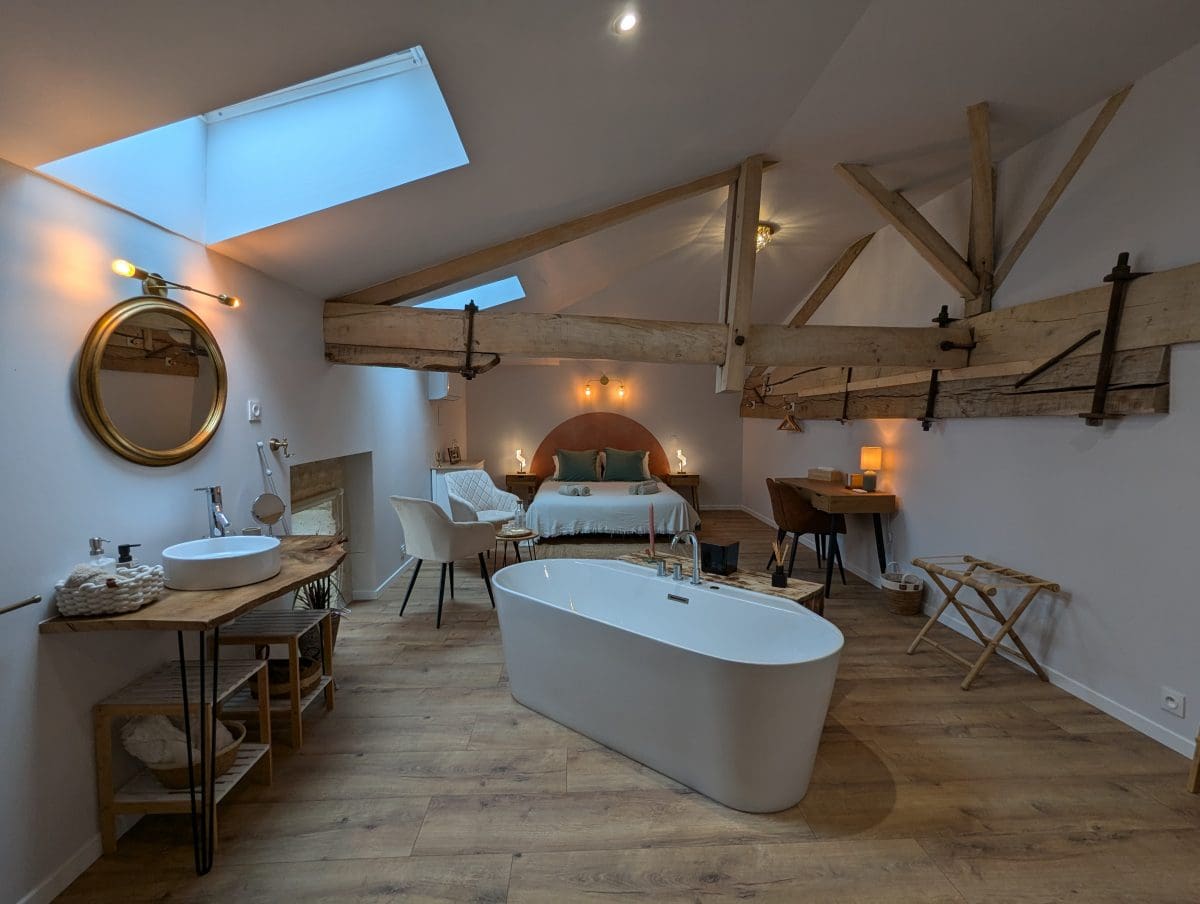 Chambre d’hôtes de charme en Charente, près d’Angoulême : poutres apparentes, parquet, baignoire îlot, double vasque, lumière tamisée.