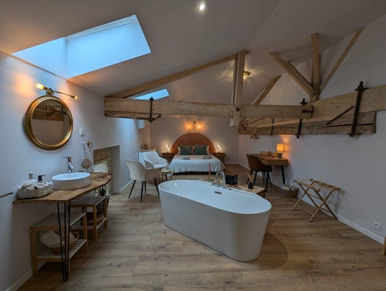 Chambre d’hôtes de charme en Charente, près d’Angoulême : poutres apparentes, parquet, baignoire îlot, double vasque, lumière tamisée.