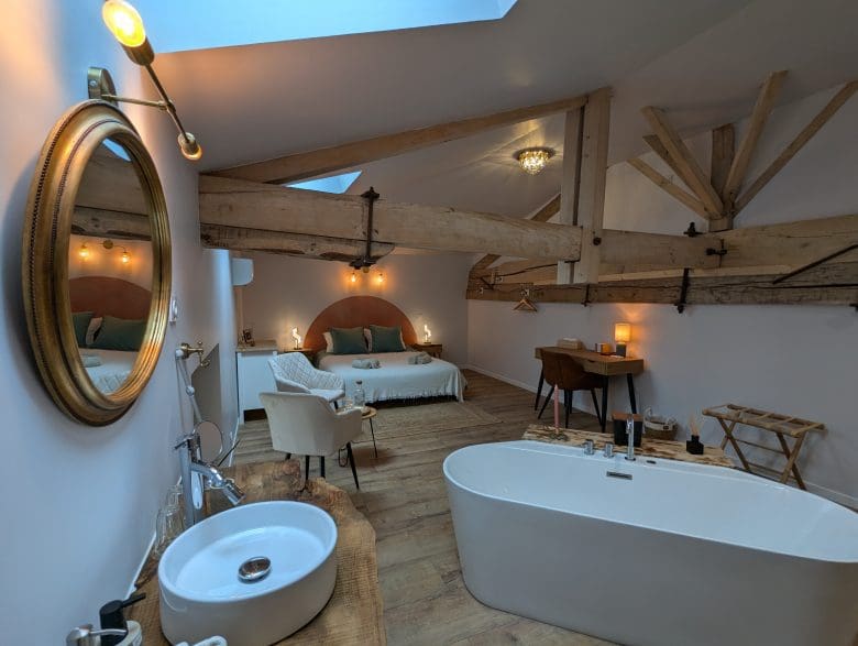 Chambre loft au charme charentais à Angoulême : poutres apparentes, lit king-size, baignoire, coin douillet sous une verrière lumineuse.