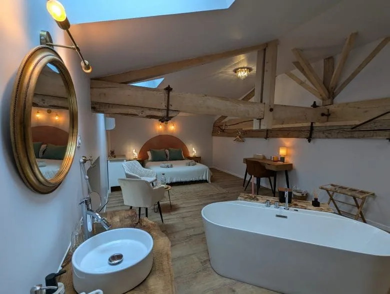 Chambre loft au charme charentais à Angoulême : poutres apparentes, lit king-size, baignoire, coin douillet sous une verrière lumineuse.