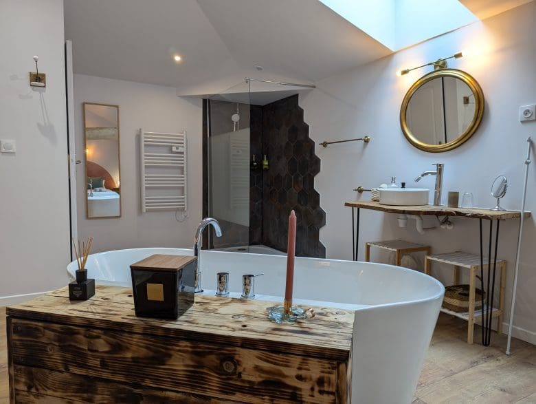 Salle de bain moderne inspirée des chambres d'hôtes de Charente, avec baignoire îlot, bois chaleureux, douche élégante et lumière zénithale.