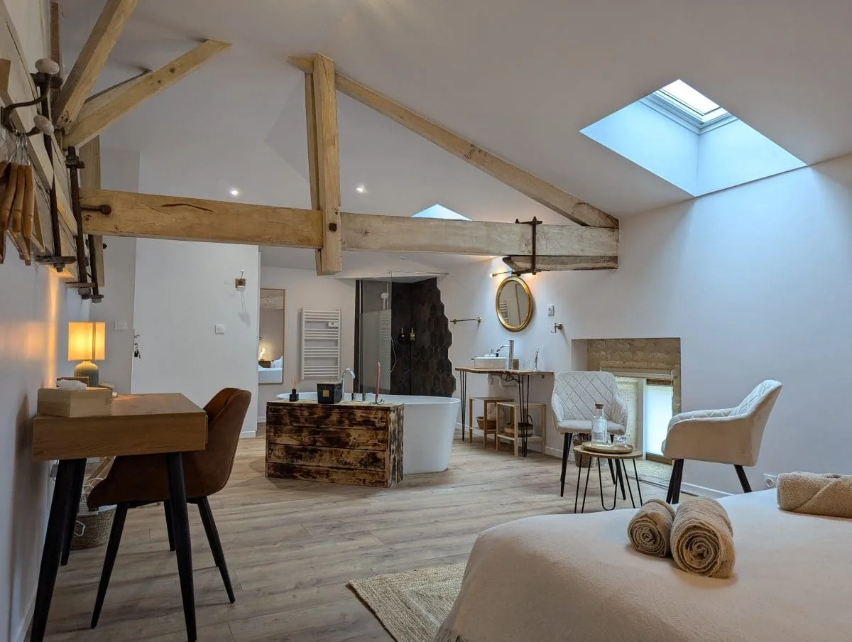 Spacieuse chambre loft à Angoulême, avec poutres charentaises, baignoire îlot, bureau en bois, lumière chaleureuse et lit douillet.