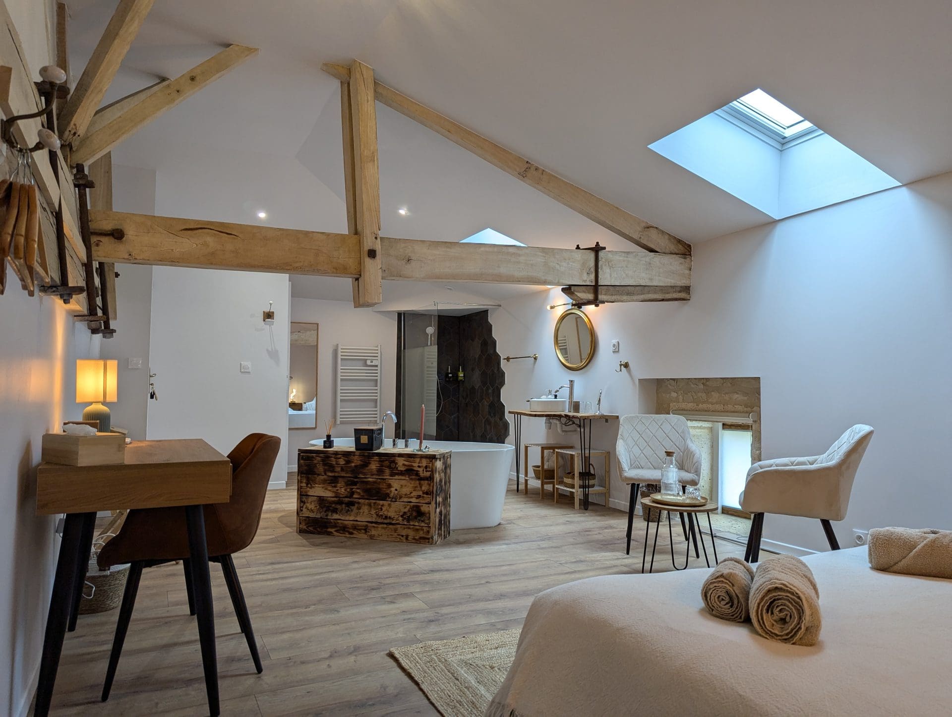 Spacieuse chambre loft à Angoulême, avec poutres charentaises, baignoire îlot, bureau en bois, lumière chaleureuse et lit douillet.