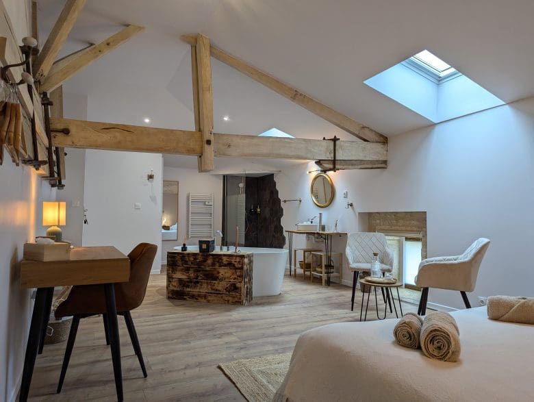 Spacieuse chambre loft à Angoulême, avec poutres charentaises, baignoire îlot, bureau en bois, lumière chaleureuse et lit douillet.