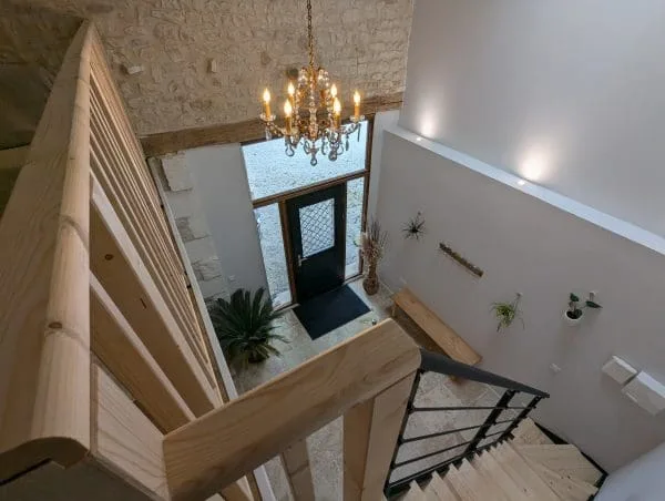 Entrée chaleureuse de style charentais à Angoulême : escalier en bois, murs en pierre, banc en bois, plantes et lustre accueillant.