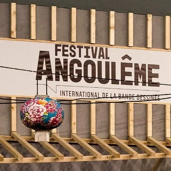 Au cœur du centre historique d’Angoulême, en Charente, une élégante enseigne annonce le Festival international de la bande dessinée, posée sur une structure en bois chaleureuse qui rappelle l’esprit convivial des maisons d’hôtes charentaises. Juste en face, une lanterne colorée éclaire l’entrée et invite à découvrir l’ambiance unique de ce festival emblématique de la région.