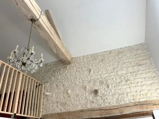 Dans une ambiance chaleureuse et conviviale, typique des chambres d’hôtes de Charente, cet intérieur plein de charme dévoile un mur en pierre authentique, des poutres apparentes en bois, un élégant lustre en cristal et une balustrade en bois mettant en valeur la mezzanine. À deux pas d’Angoulême, ce décor raffiné incarne l’art de vivre charentais, alliant tradition et confort moderne.
